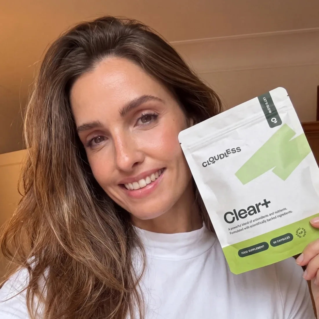 Una mujer sonriente con una piel más limpia sostiene Clear+