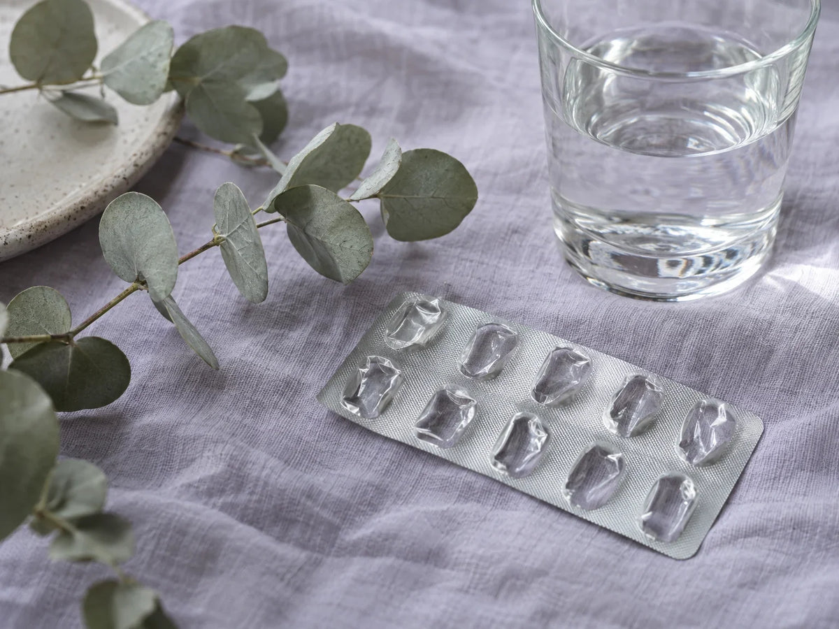 Lege pilstrip naast eucalyptus en een glas water op lila linnen